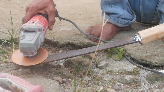 A man is sharpening a traditional machete blade using an electric hand grinder outdoors.