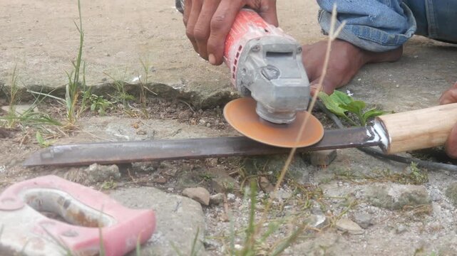 A man is sharpening a traditional machete blade using an electric hand grinder outdoors.