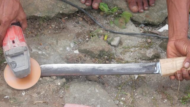 A man is sharpening a traditional machete blade using an electric hand grinder outdoors.