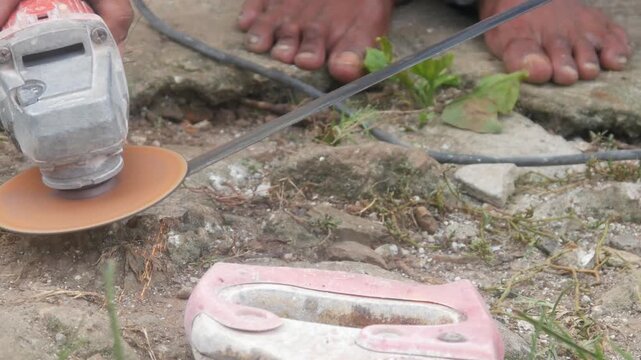 A man is sharpening a traditional machete blade using an electric hand grinder outdoors.
