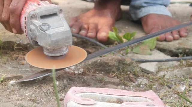A man is sharpening a traditional machete blade using an electric hand grinder outdoors.