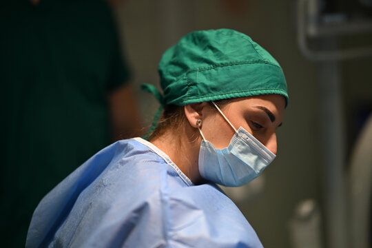Female Surgeon Wearing Surgical Mask and Scrub Cap Focused During Operation in Hospital