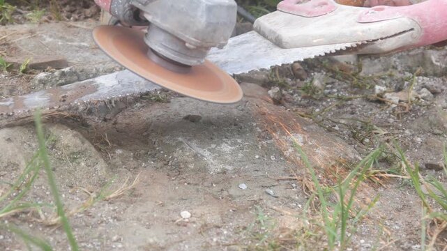 Workers are sharpening or cutting saw blades using a hand grinder in an open area.
