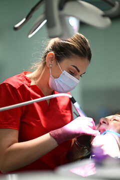 Female Dental Hygienist Wearing Mask and Gloves Performing Dental Cleaning on Patient in Clinic