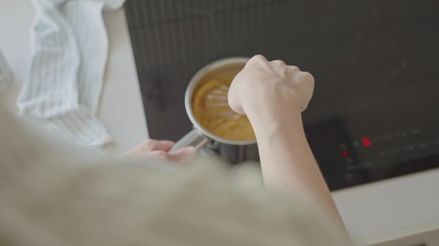 Woman stirs mixture with whisk in saucepan on induction cooktop