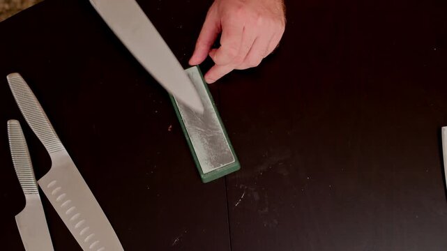 Hands sharpening a large kitchen knife with a stone on a dark table