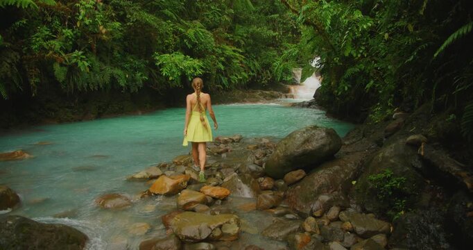 Woman walking across rocky stream toward Blue Falls pool on a vibrant summer trip in Costa Rica