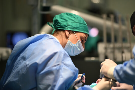 Female Surgeon Operating With Surgical Team Wearing Mask and Scrubs in Hospital Operating Room