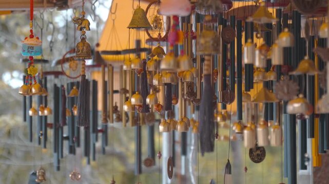 A multitude of shiny gilded tubular wind chimes with bells and engraved Hindu Om signs hang in a row and sway in the wind, producing melodic sounds
