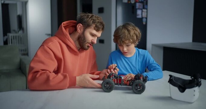 Father and son assembling a small robotic car at home, exploring electronics, wheels, wires, and hands-on STEM learning together