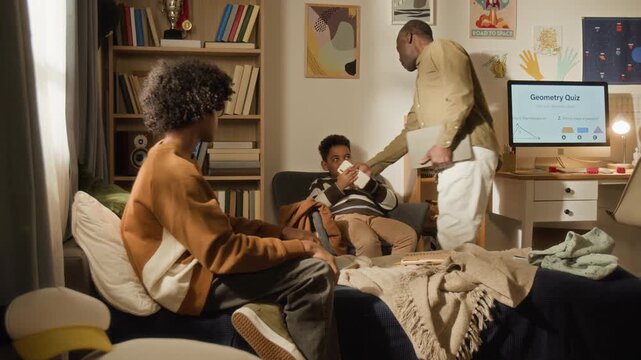 Medium shot of annoyed, strict African American father removing digital gadgets from kids for exceeding daily screen time, ordering to clean mess in bedroom, exercising parental control and authority