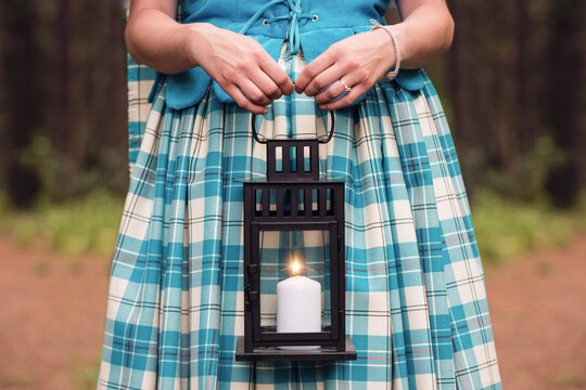 Highland dancer in blue Aboyne dress holding lit candle lantern in forest
