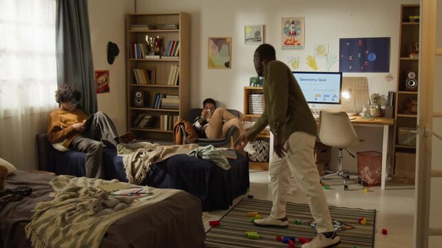 Wide shot of two African American brothers relaxing in bedroom, using digital gadgets, father walking in, stumbling over construction blocks on floor, confiscating smartphone and tablet for discipline