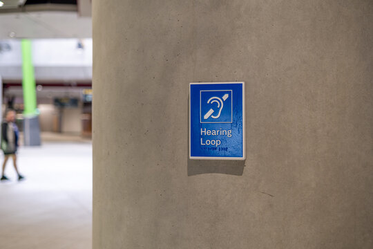 A blue hearing loop (audio induction loop) sign at concourse inside Anzac Station on Melbourne's Metro Tunnel line in Australia. International accessibility symbol for hearing impairment 