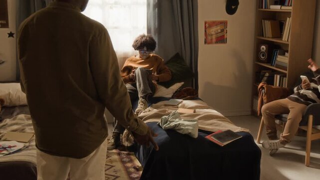 Medium full follow shot of black father walking into boys bedroom, shouting at sons for mess in bedroom, ordering to clean up and removing smartphone and tablet as punishment, gadget addiction concept