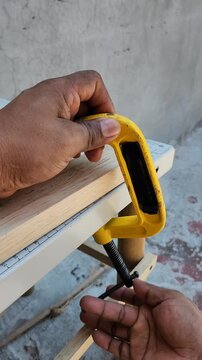 Hand removing a metal F-clamp from a wooden board piece