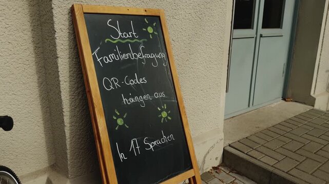 Informational chalkboard sign at the entrance of a public kindergarten in Berlin mentioning family survey participation and QR codes available in 17 languages. Concept of multicultural education.