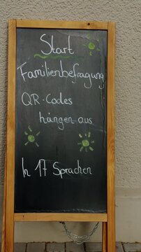 Handwritten chalk message outside a Berlin state kindergarten announcing multilingual family participation with QR codes in 17 languages. Diversity and inclusive education concept in Germany.