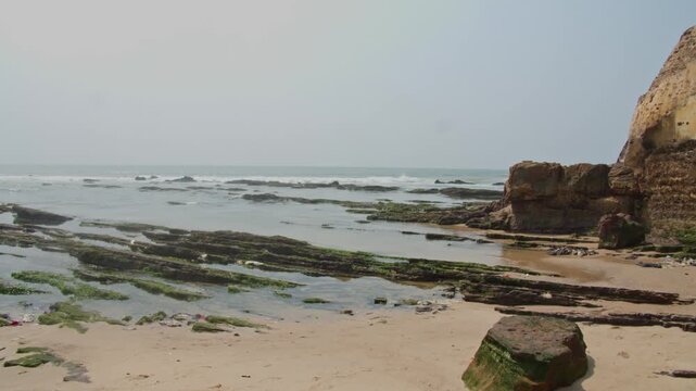 Gentle atlantic ocean waves washing over mossy rocks on sandy Kokrobite beach near Accra, Ghana, coastal erosion on nearby sandstone cliffs and sea level