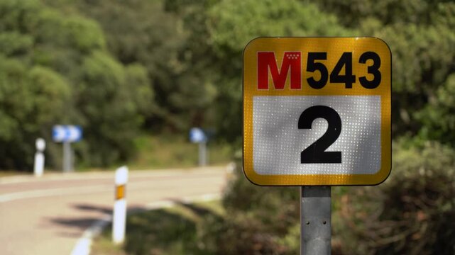 Carretera comarcal de la Comunidad de Madrid con coches circulando, se&ntilde;al de tr&aacute;fico y punto kilom&eacute;trico junto a la calzada.