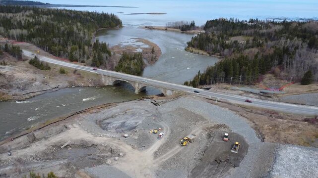 Scenic drone view of the Arthur-Bergeron coastal bridge, heavy machinery, wooded shoreline, and construction activity along the Mitis River in Gasp&eacute;sie, Quebec, Canada, 2026