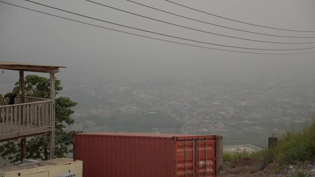 Overlooking Accra in Ghana showing a red cargo container and hazy skyline with power lines and urban sprawl during a dusty harmattan season in West Africa