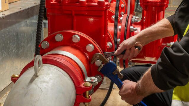 Fire system and specialist sprinkler engineer using wrench and ratchet to tighten a red pipe flange. Residential building fire and safety planned maintenance