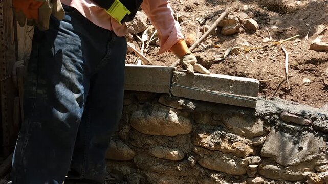 Young mason securing a concrete block onto a solid stone foundation