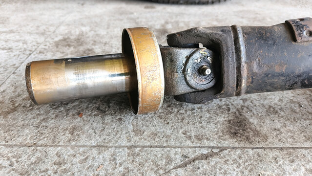 Close-up of a dirty automotive driveshaft slip yoke and universal joint on a floor. Used metal car part for drivetrain maintenance and vehicle repair.