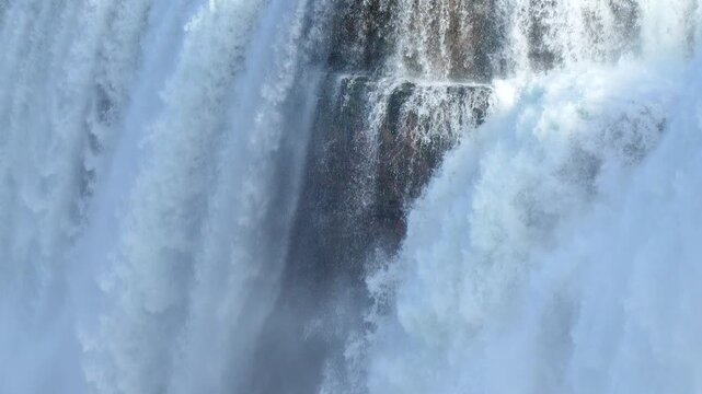 Waterfall cascading over dark rocky cliffs with powerful splashing white foam and mist in 120fps 4K Slow Motion