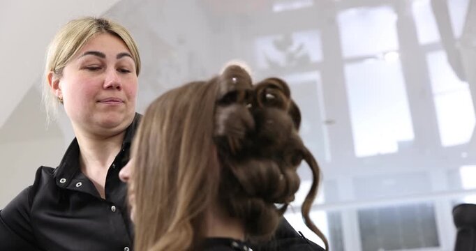 Hairdresser styling woman's hair in beauty salon, closeup