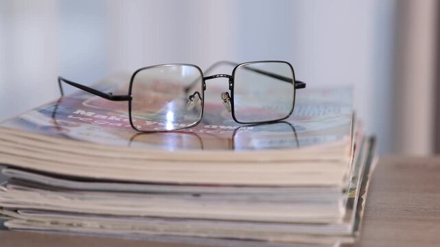 Many lifestyle magazines and glasses on wooden table, closeup. Camera moving forward