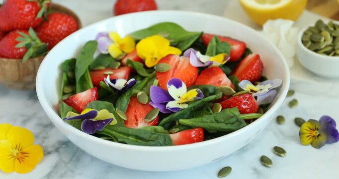 Woman adding pansy flower to delicious salad at table, closeup