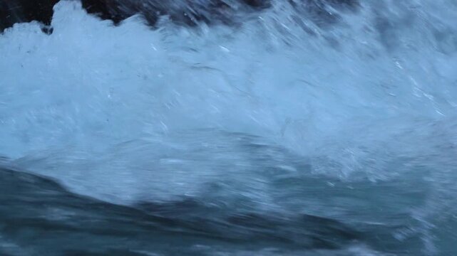 River water rushing through a rocky stream with splashing white foam and deep blue currents in 120fps 4K Slow Motion
