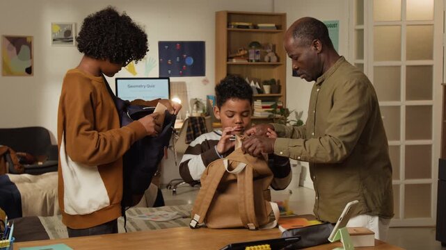 Medium shot of caring African American father sending two sons to school in morning, packing schoolbags and lunch, then giving pocket money in cash dollars, for financial literacy in young age