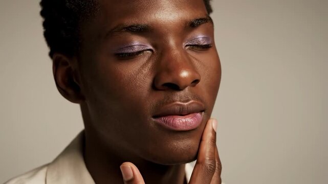 A man with dark skin and short hair covers his face with his hand, conveying a sense of modesty or vulnerability.