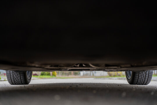 Low angle view of a car underbody and front tires on asphalt road, showing ground clearance, suspension components, and tread pattern of the vehicle.