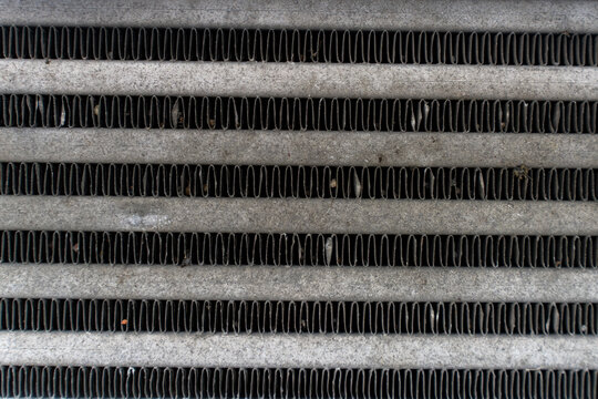 Close up of a dirty car radiator or intercooler aluminum fins with accumulated dust and debris, showing automotive cooling system texture and maintenance requirements.