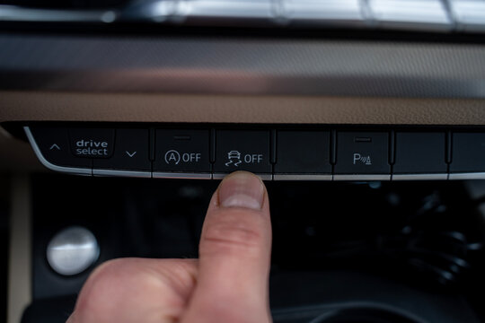 Close up of a finger pressing the traction control off button on a modern car's dashboard console to disable electronic stability control, located among other functional switches.