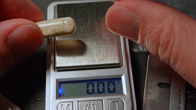 Concept drug dealer measure powder of synthetic opioid drug of fentanyl in the gelatin capsule for sale on the streets or parties, using electronic scale. Educational concept of toxic drug crisis
