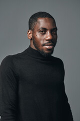 Obraz premium African man with dark skin wearing black turtleneck sweater posing in studio with neutral gray background creative conceptual visual style portrait of confident male model.