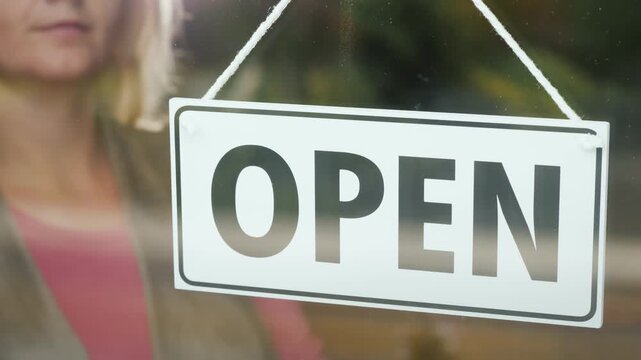 Woman flips open sign to closed on glass door of shop during day.