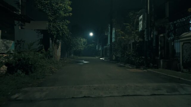 Color graded dimly lit empty suburban street alley at night with bright single street lamp casting eerie green shadows