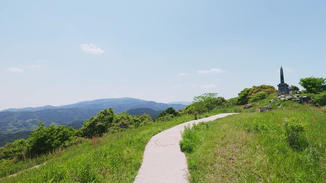 基山山頂の緑豊かな丘へと続く遊歩道と青空に映える記念碑（佐賀県基山町）