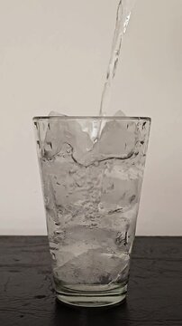 Chorro de agua pura llenando un vaso alto repleto de cubos de hielo picado