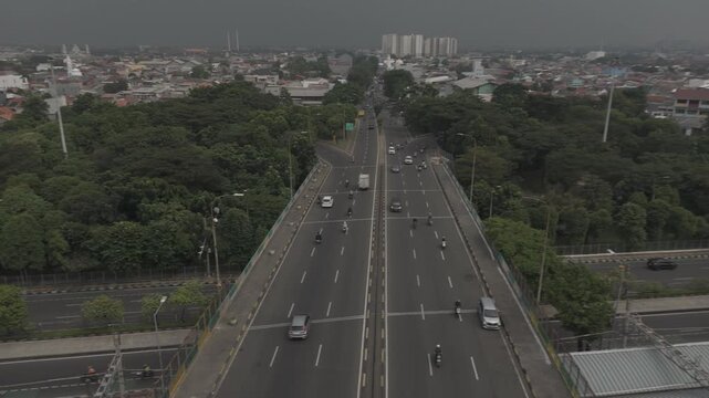 Shot in D-Log M Aerial view of a highway bridge overpass with vehicle traffic leading toward a distant city skyline under overcast skies