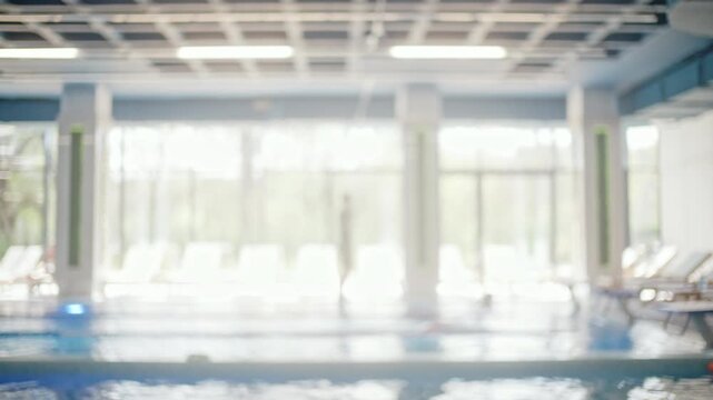 Blurred view of people training in an inside swimming pool with panoramic windows in the background