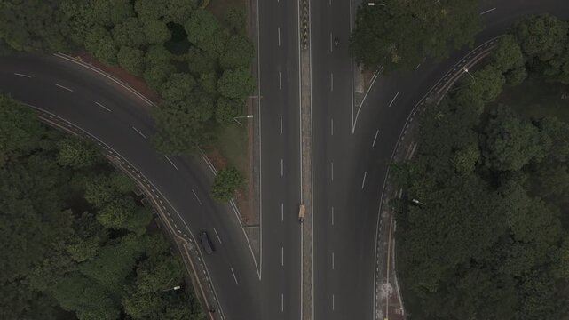 Top down aerial view of highway split with vehicles driving through lush green trees on asphalt road