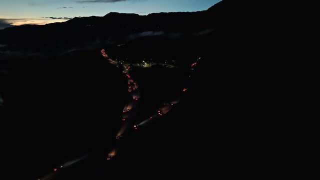 Night aerial view pulling back diagonally from Rodovia dos Imigrantes highway traffic with vehicle taillights, mountain silhouette and twilight sky at Santos, Brazil. Pull back camera movement