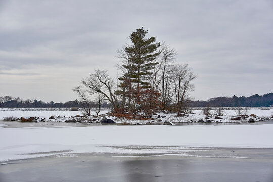 Island with trees on it, in the middle of a frozen snow covered lake.